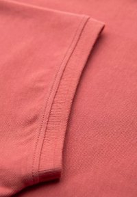Koralinvärgad tyg med en slät textur, med ett ribbat manschettdetalj. Närbilden visar väv och sömnad av textilen.
