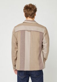 Giacca a righe marrone e beige con colletto, polsini a bottoni e un gancio sul retro. Realizzata in un tessuto testurizzato, presenta una vestibilità su misura.