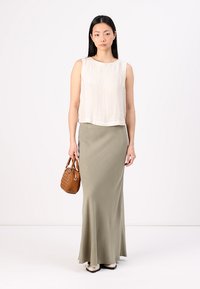 Top senza maniche beige chiaro e una lunga gonna verde oliva, abbinati a una piccola borsa intrecciata marrone e scarpe beige.