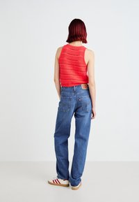 Rode gebreide crop top met open werkpatronen, gecombineerd met high-waisted blauwe jeans en witte sneakers met rode strepen.