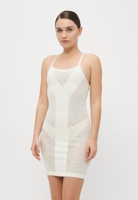 Vit nätklänning med justerbara spaghettiaxlar, figurnära design och geometriska utskärningar. Slät, stretchigt tyg med en elegant textur.