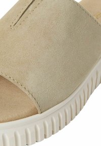 Beige suède slipper sandaal met een brede band, open tenen ontwerp, en een witte textuurzool met een geribbeld patroon.