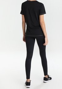 Svart atletisk t-shirt med korta ärmar och kontrasterande sömmar, tillsammans med svarta leggings med nätpaneler och en figurnära design.