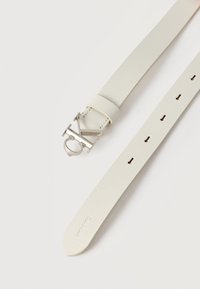 Λευκή ζώνη από δερμάτινη υφή με ασημένια μεταλλική αγκράφα σε σχήμα διπλών διαπλεκόμενων γραμμάτων "C" και "K", με έξι ορατές τρύπες ρύθμισης.