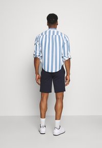 Světle modrá a bílá pruhovaná košile s ohrnutými rukávy, v kombinaci s tmavě námořnickými pruhovanými šortkami. Bílá teniska dokončuje outfit.
