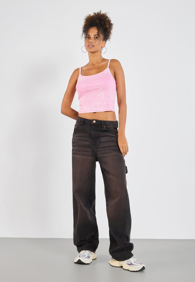 Ljusrosa ribbad crop top som kombineras med högmidjade svarta vida jeans. Modellen bär sneakers och stora hoopsörhängen. Neutral bakgrund.