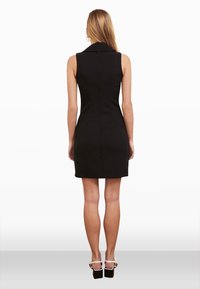 Robe noire sans manches avec un col, design ajusté, coupe au genou, texture lisse et sans motifs visibles. Portée avec des sandales noires à talons carrés.