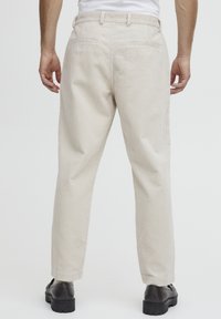 Light beige corduroy trousers with vertical ribbed texture, straight cut, two back pockets, and worn with black shoes.