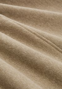 Tan stof met een gladde textuur, met subtiele variaties in kleur en patroon, gerangschikt in zachte plooien en kreukels.