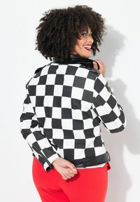 Veste de moto en cuir à carreaux noirs et blancs avec un col noir et des zips, au design ajusté, associée à un pantalon rouge.