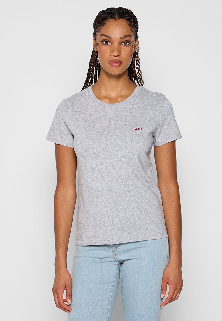 T-shirt en coton gris à manches courtes, col rond, avec un petit logo rouge sur la poitrine gauche. Associé à un jean bleu clair.