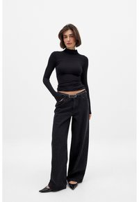 Black long-sleeve fitted top, paired with loose black jeans featuring a subtle pattern, and black pointed-toe flats.