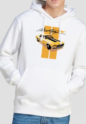 Weißer Hoodie mit gelbem Vintage-Mustang-Auto-Grafik und schwarzem "Mustang"-Schriftzug, getragen von einer Person mit den Händen in der Bauchtasche.