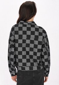 Svart och grå rutig flanelljacka, med krage, långa ärmar, boxig passform, knapppdetaljer vid ärmsluten och en denimliknande textur.