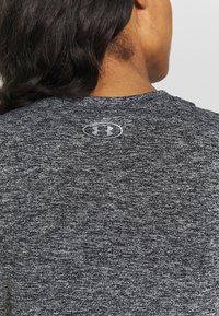 Grå atletisk t-shirt med melerad textur, med en silverlogga vid bakhalsen. Enkel, ventilerande tyg.