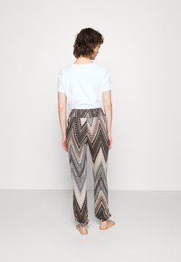 Tiskane hlače s zigzag vzorcem v nevtralnih tonih, z elastičnim pasom in zaprtimi robovi. V kombinaciji z osnovno belo majico.