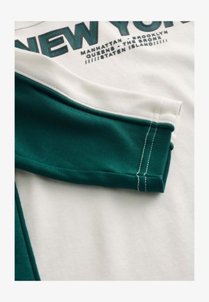 T-särk rohelise ja valge mustriga, millel on tekst "NEW YORK." Valmistatud pehmest puuvillast, eristuvad kontrastsed värvid ja nähtav õmblus.