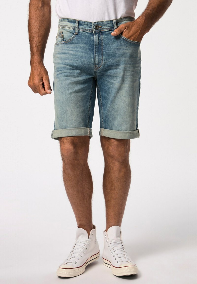 Pantalones cortos de mezclilla azul claro, con dobladillos enrollados, cinco bolsillos y cierre de botón. Combinados con zapatillas altas blancas.