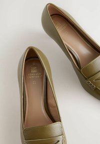 Rohelised nahast loafers, millel on sile tekstuur, ümar peaks ja dekoratiivne tikand. Sees on pruuni voodriga, millel on "Igavene Mugavus" bränd.