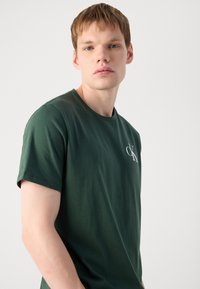 Mørkegrøn crew neck t-shirt lavet af blødt stof, med et lille hvidt logo på brystet. Korte ærmer med en afslappet pasform.