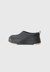 Fekete slip-on cipő sima gumiból, kerek orral, kiemelkedő sarkal és fehér texturált talppal. Hátul hurokkal a könnyű felhúzás érdekében.