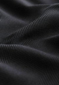 Schwarzer Textilstoff mit einem Fischgrätmuster, das durch markante Linien besticht und das weiche, gewebte Erscheinungsbild sowie die reiche Farbtiefe betont.