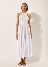 Abito maxi bianco a strati con collo halter e corpetto in pizzo. Tessuto leggero, silhouette fluida, indossato con sandali piatti marroni.