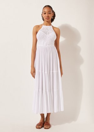 Weißes, gestuftes Maxikleid mit Halterhals und Spitzentop. Leichter Stoff, fließende Silhouette, getragen mit braunen Flachsandalen.