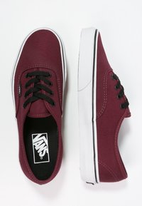 Burgunderrote Canvas-Sneaker mit schwarzen Schnürsenkeln, weißen Gummisohlen und Vans-Logo auf der Innensohle. Klassisches Low-Top-Design mit sichtbaren Nähten.