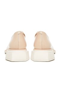 Paire de mocassins en cuir beige vus de dos, avec des semelles blanches épaisses à motifs géométriques et des détails de couture.