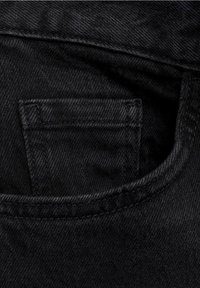 Gros plan d'une petite poche à monnaie en denim noir à l'intérieur de la poche avant d'un jean noir, montrant les coutures détaillées et la texture du tissu.