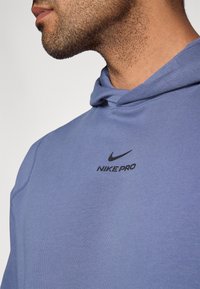 Φούτερ με κουκούλα σε ανοιχτό μπλε υλικό, με μαύρο λογότυπο Nike Pro στο στήθος. Με ομαλή υφή και άνετη εφαρμογή.