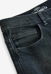 Donkerdenimjeans met een enkele voorklepzak, voorzien van een gestikte naad en metalen knoopaccenten, met een gladde, licht gestructureerde oppervlakte.