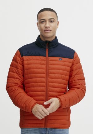 Red puffer jacket with a navy blue upper section, featuring a high collar and zip closure. Horizontal quilted texture throughout.