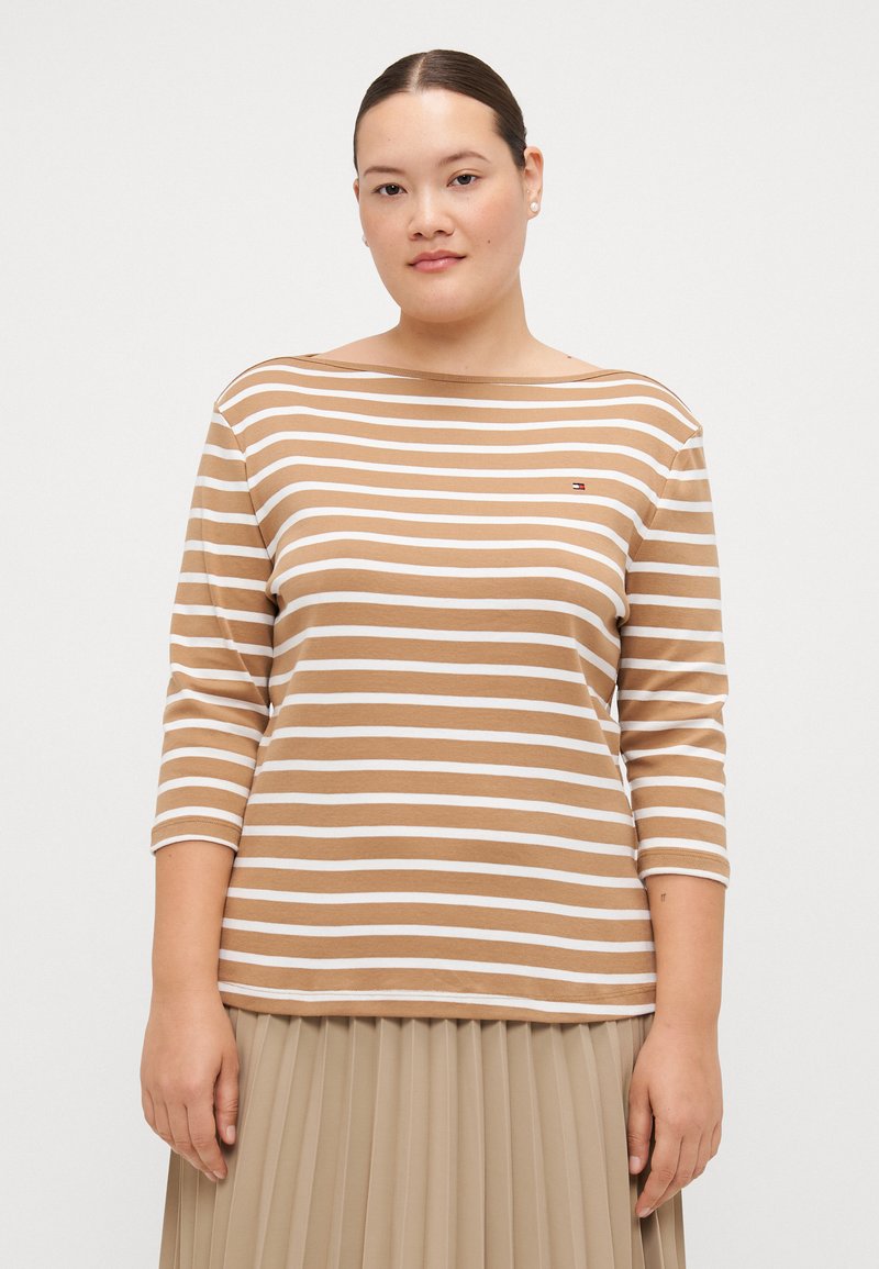 Camiseta de manga larga en rayas marrones y blancas, con un diseño de cuello barco y un pequeño detalle del logo en el pecho. Fabricada en un tejido suave y elástico.