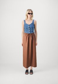 Denim crop top med knapfront, parret med en lang, brun, elastisk taljeskirt. Sorte open-toe mules fuldender outfittet.
