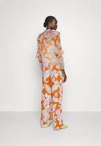 Jumpsuit floreale arancione con motivi rosa e bianchi. Presenta maniche arricciate e pantaloni larghi e svasati. Texture liscia.