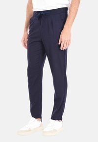 Pantaloni navy con vita regolabile, frontale plissettato e tasche laterali. Indossati con sneakers bianche, caratterizzate da una finitura testurizzata.