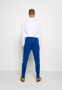 Pánské sportovní oblečení s bílou dlouhou rukávem a modrými kalhotami se bočními pruhy, vyrobené z elastické tkaniny a navržené pro pohodlí.