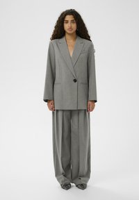 Szary garnitur w paski składający się z dwurzędowej, oversize'owej marynarki z jednym guzikiem oraz szerokich spodni o luźnym kroju.