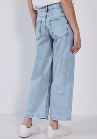 Jean ample bleu clair en denim, avec poches arrière et décoloration subtile. Associé à des baskets blanches, offrant un look décontracté.