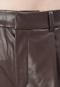 Close-up of brown leather pants waistband with belt loop and gathered stitching detail.
