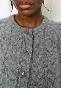 Halli hallitatud kardigan, millel on kaabelmustrit, ümmargune kaelus ja kolm tumehallide nupuga kinnitust. Pehme, tekstuuriga kangasteave nähtav.