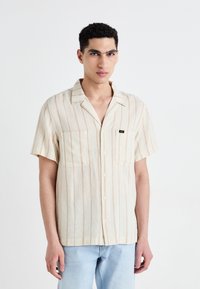 Short-sleeve button-up shirt in light beige with vertical pale orange stripes. Features two chest pockets and a collar detail.