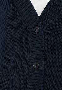 Tengerészkék kötött kardigán mély V-nyakkal, bordás textúrával és három fekete gombbal az elején.