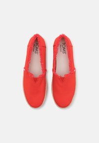 Røde kanvas slip-on sko med frynsete kanter, med en lys brun jutesål og en teksturert overdel. Merking synlig innvendig.
