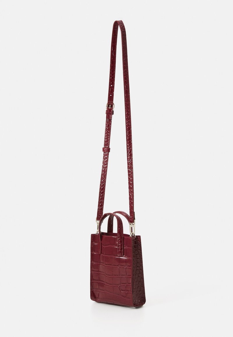 Small burgundy handbag with a crocodile embossed pattern, two short handles, and a long adjustable strap. Smooth texture.