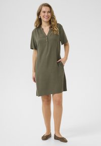 Robe courte olive à manches courtes avec patte de boutonnage et poches latérales. Fabriquée en tissu doux, de coupe droite, longueur genoux, finition texturée.