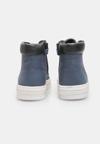 Bottines en cuir bleu avec des accents noirs, dotées d'une fermeture à glissière et d'une semelle en caoutchouc blanche. Texture lisse et forme arrondie.