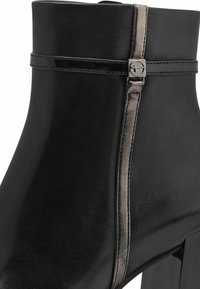 Bottine noire avec une finition en cuir lisse, dotée d'une bande métallique et d'une fermeture éclair sur le côté. Le talon épais offre de la stabilité.